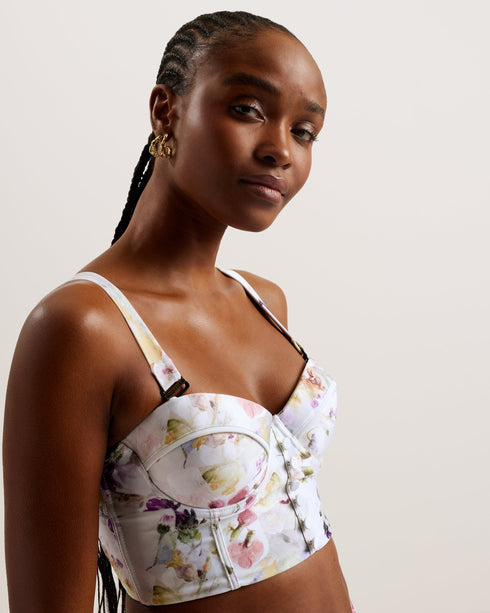 ULANIA-Swimwear-The ULANIA bikini top makes for sweet swimwear with a pressed floral print and faux button detailing down its longline design. Underwire and padding on the bust create a flattering and supportive fit, with removable straps for versatile style. It fastens at the back with a branded hook, finished with a playful cut-out detail. Longline bikini top Pressed floral print Faux button detail Back cut out Padded cups with underwire Removable and adjustable straps Hook fastening Lydia is 5'10" / 1.77